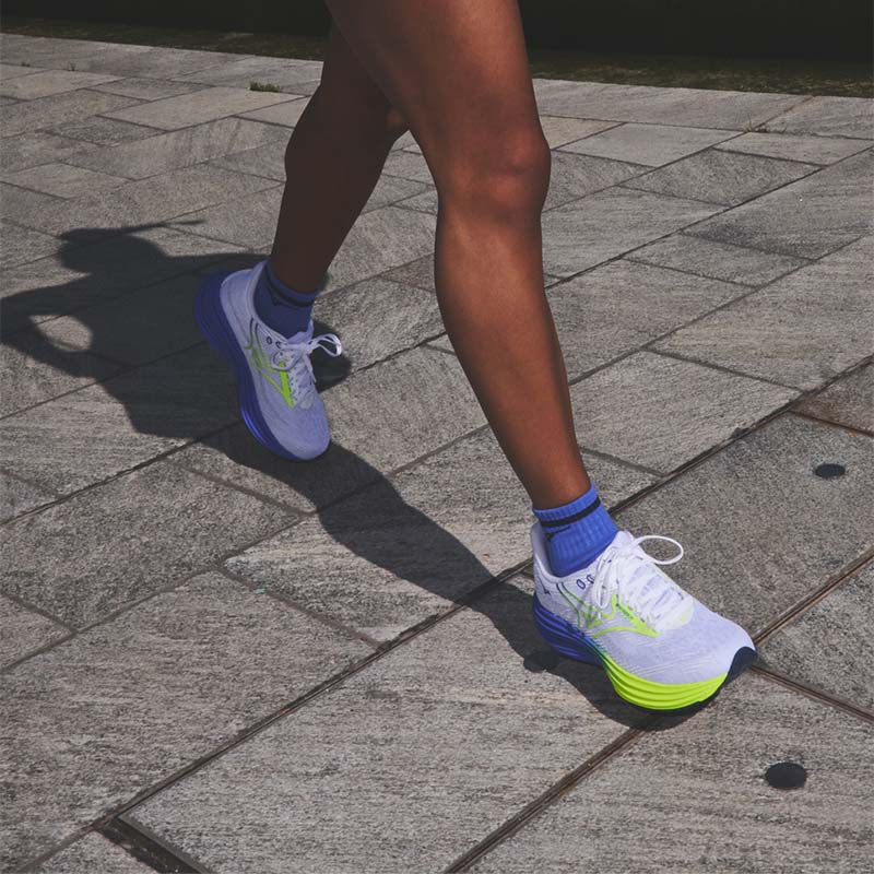 Runner wearing white Mizuno Wave Rider 29 running shoes with green-yellow and blue accents on a sidewalk 