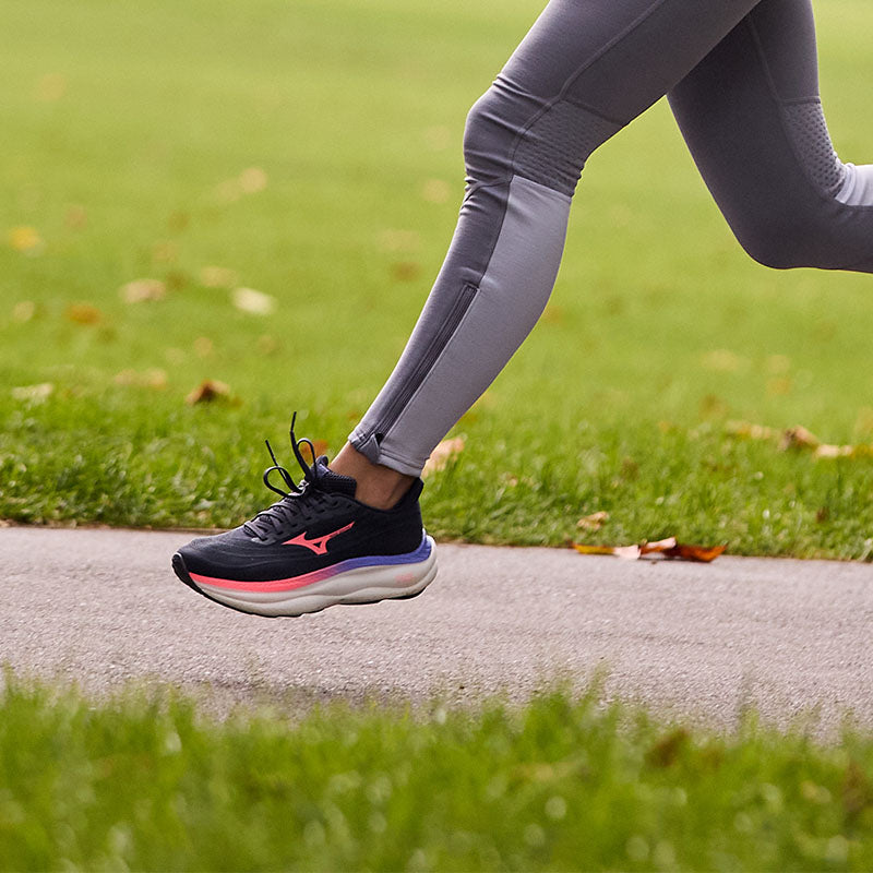 Person running outdoors wearing black Mizuno Wave Sky 9 running shoes with pink accents on a paved path.
