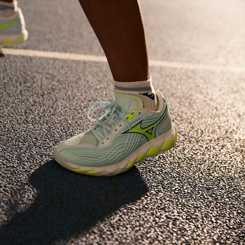 Closeup of a tennis player wearing Mizuno Wave Enforce Tour 2 AC shoes on a hard court surface