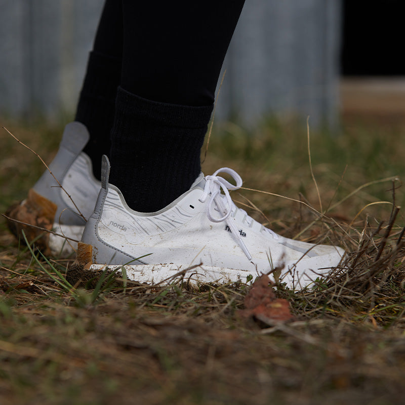 Person wearing white norda 001 trail running shoes on grass