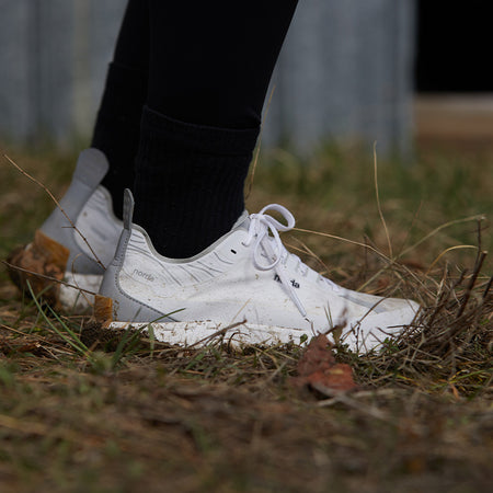 Person wearing white norda 001 trail running shoes on grass