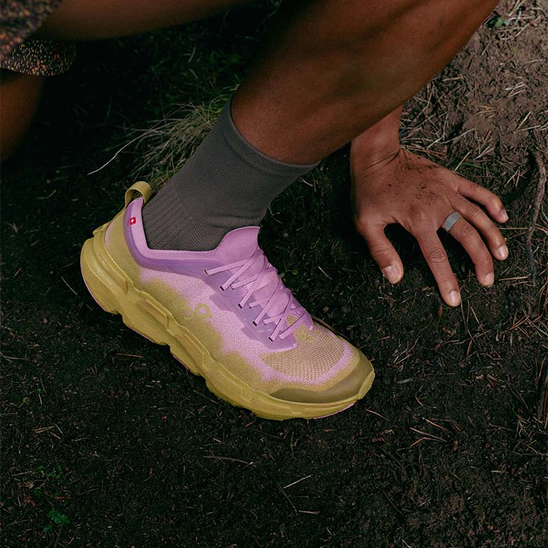 A person running a dirt trail in pink, purple and tan On Cloudsoma trail running shoes 