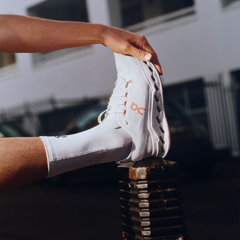 Person wearing white On Cloudsurfer Max running shoes with orange accents