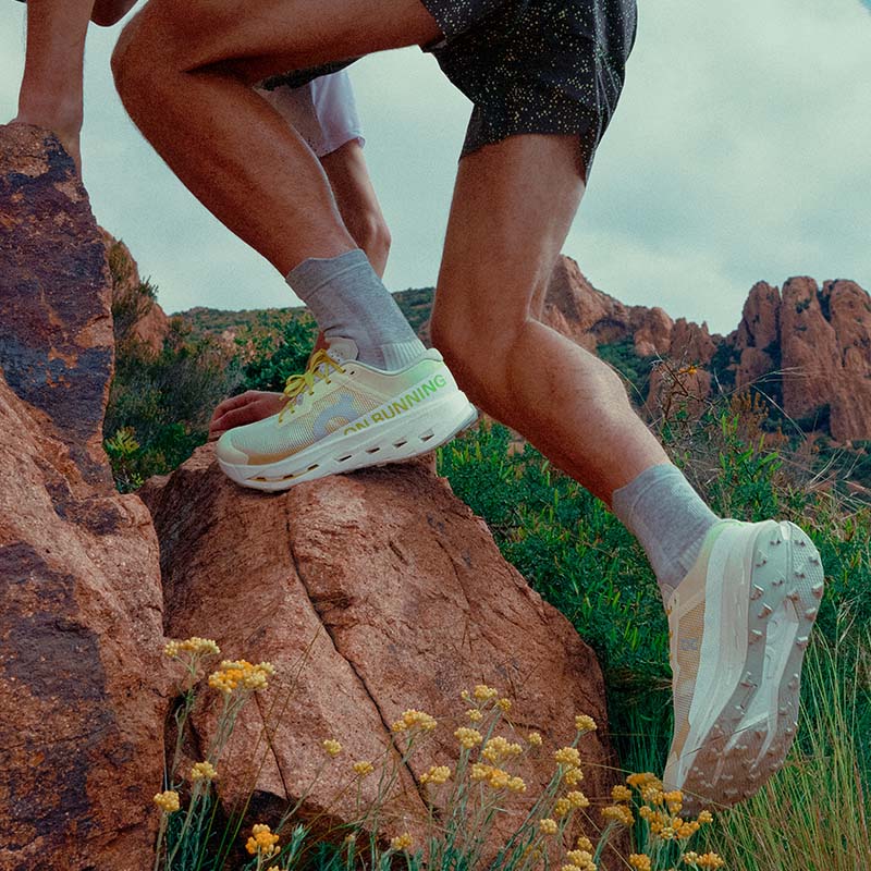 Person wearing yellow On Cloudultra Pro running shoes with white accents on a rocky landscape