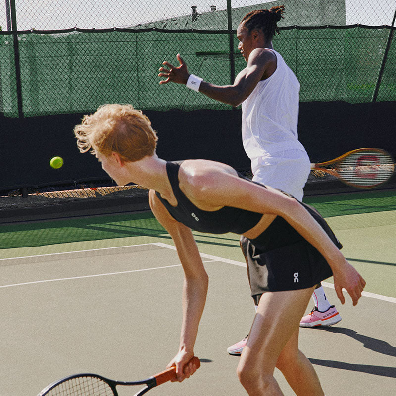 Two tennis players in action wearing On Court clothing with a green fence in the background.