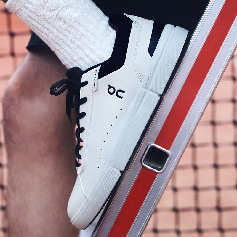 White On The Roger Advantage lifestyle sneakers with dark blue accents worn on a tennis court