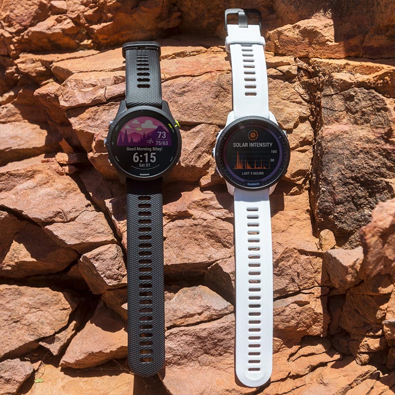 A black and a white Garmin Forerunner GPS watch laying flat on red rocks in the sun.