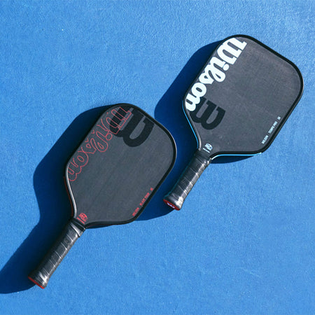 Two Wilson pickleball paddles laying flat on a blue court surface.