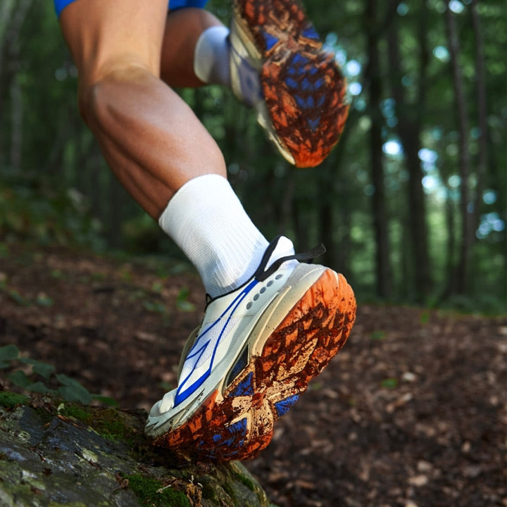 Lifestyle image: A person running a forest trail in white and blue Diadora running shoes.