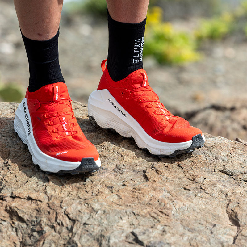 person standing on a rocky surface wearing red and white Salmon S/Lab Ultra Glide 2 Unisex trail running shoes