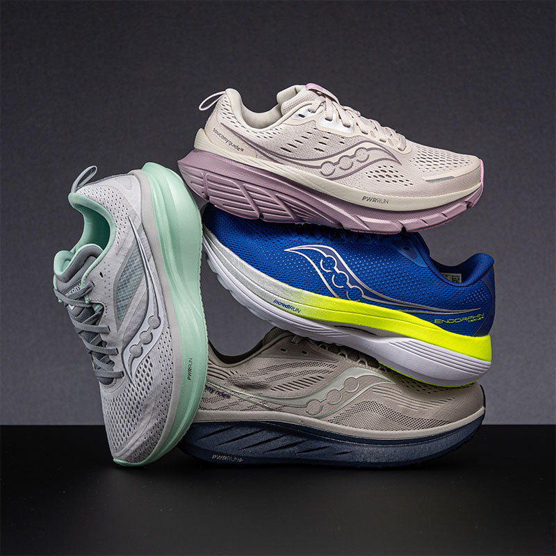 Stack of four different colored Saucony running shoes on a dark background