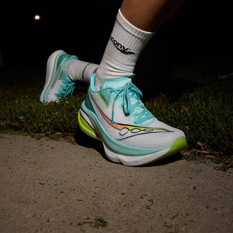 Person stretching in Saucony Endorphin Azura running shoes on a grassy area at night.