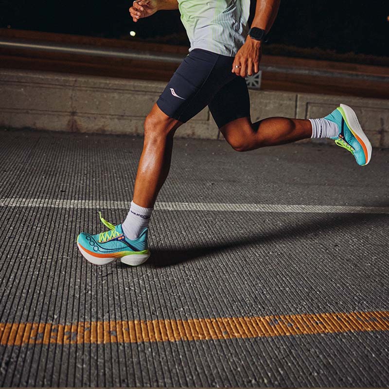 Person running on a road at night wearing Saucony Endorphin Elite 2 running shoes and shorts.