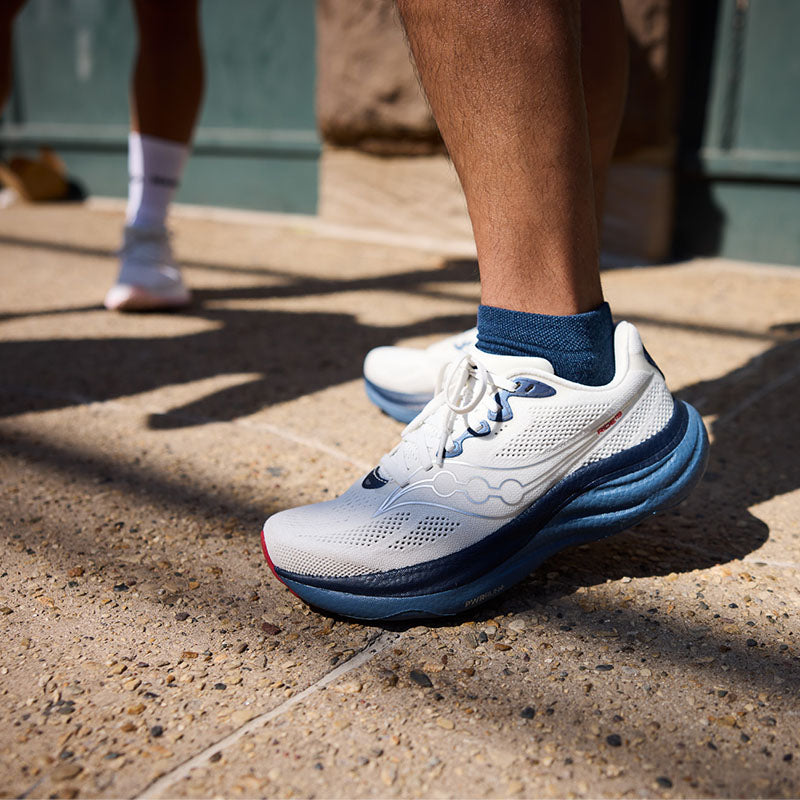 White and blue Saucony Ride 19 running shoes on a person's feet on a concrete surface.