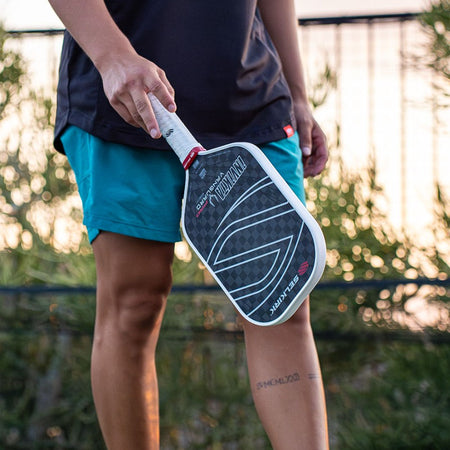 Person holding a Selkirk pickleball paddle with a blurred outdoor background