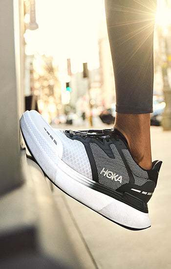A person wearing black and white HOKA Transport X running shoes