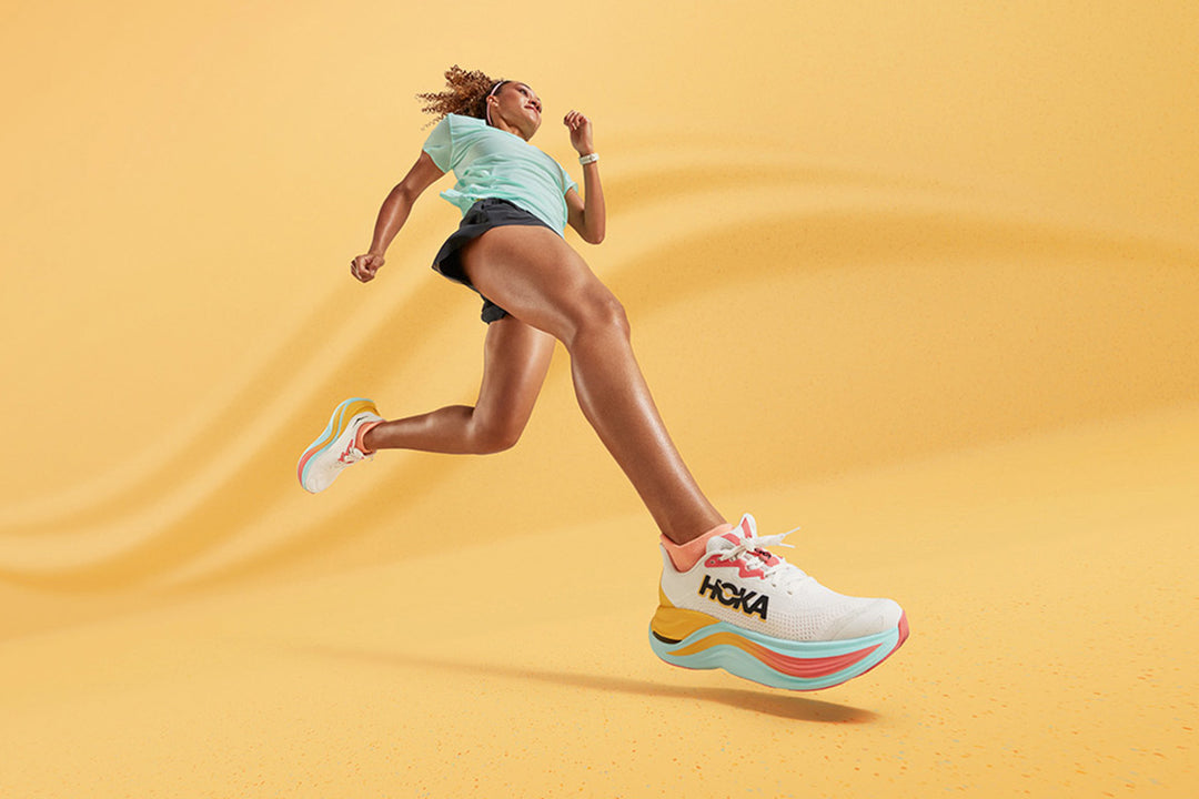A woman running while wearing the Hoka Skyward X shoe, set against a colorful background, emphasizing the shoe's dynamic performance and vibrant energy.