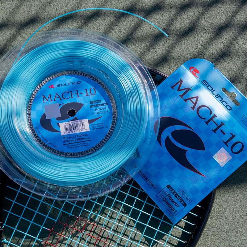 One reel and one set of Solingo MACH-10 tennis string in bright blue, placed on top of a tennis racquet on a tennis court surface.