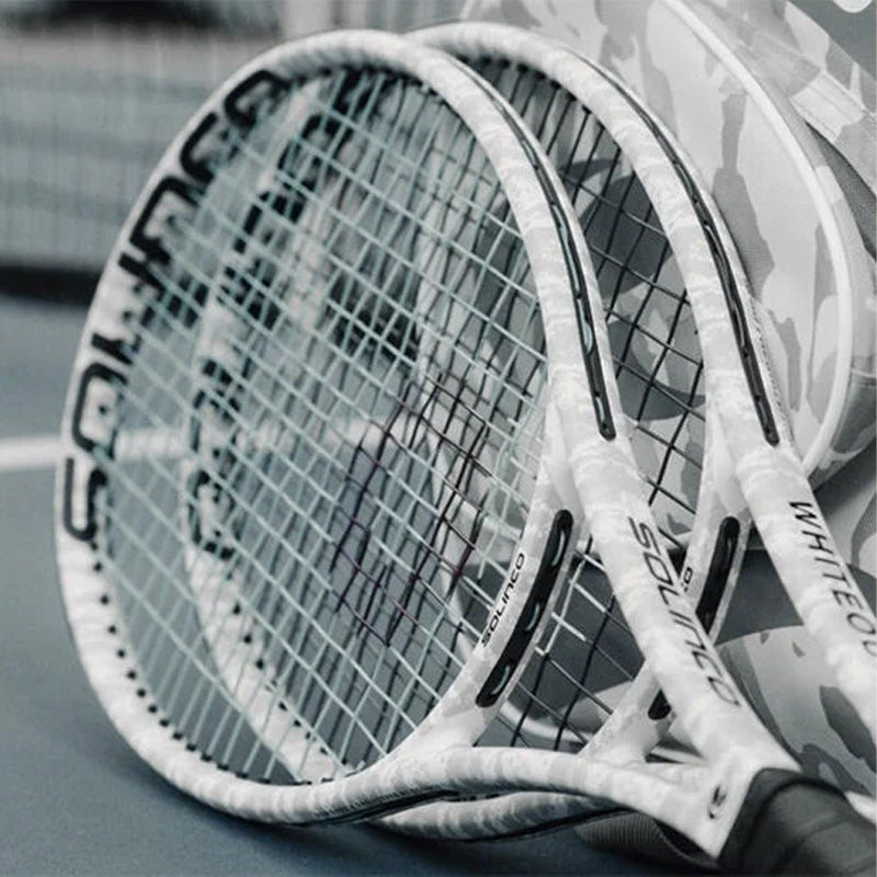 Solinco Whiteout v2 tennis racquets leaning against a matching bag on a tennis court.