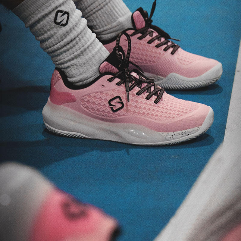 Pink Stria Sports G1 Pro pickleball shoes with black laces and a white sole, worn with white ribbed crew socks on a blue court surface.