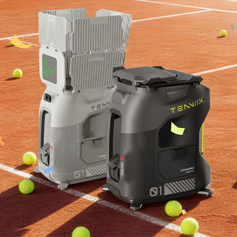 Two Tenniix tennis/padel ball machines, one light-colored and one dark, positioned on a clay tennis court with tennis balls scattered around them.