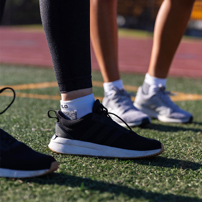 Two people wearing running shoes with Thorlo running socks on a green turf surface with a blurred all-weather track in the background