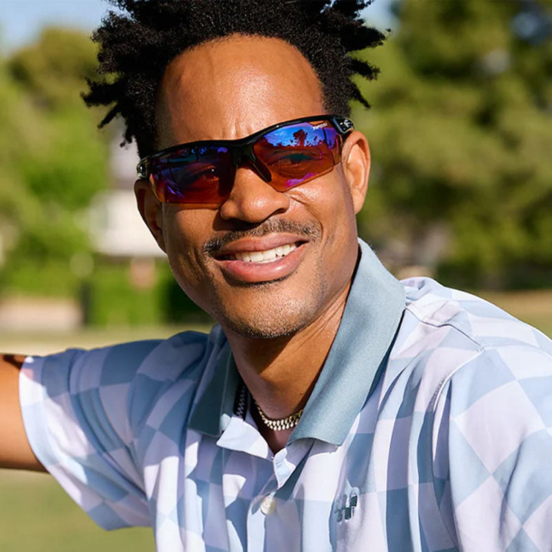 A person wearing Tifosi Vavar FC Sunglasses with black frames and AC red lenses on a golf course 