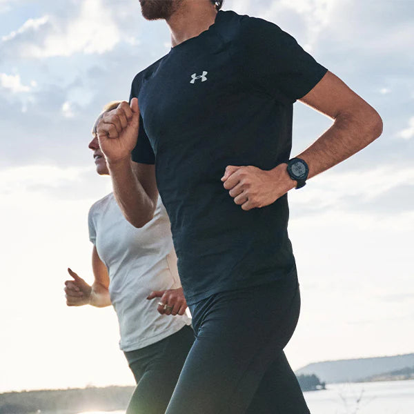 man with black under armour shirt and woman with white under armour shirt running