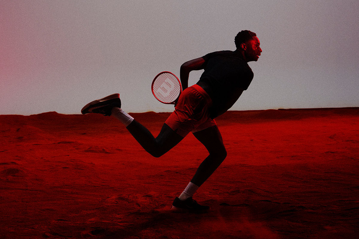 Tennis pro Moise Kouame playing with a Wilson Defyer racquet in a red-tinted desert setting